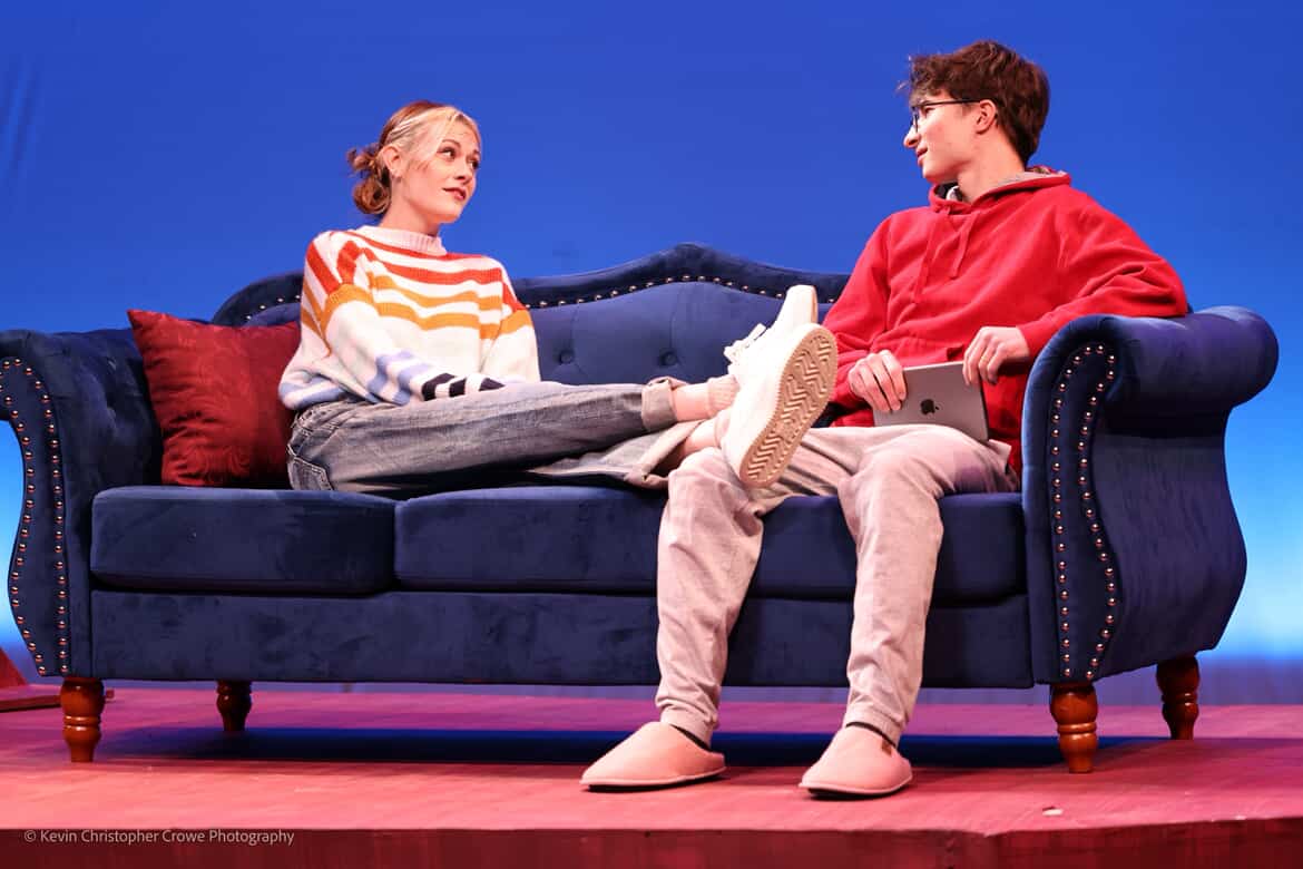 actors sit on couch on red platform. there is light blue cyc lighting.